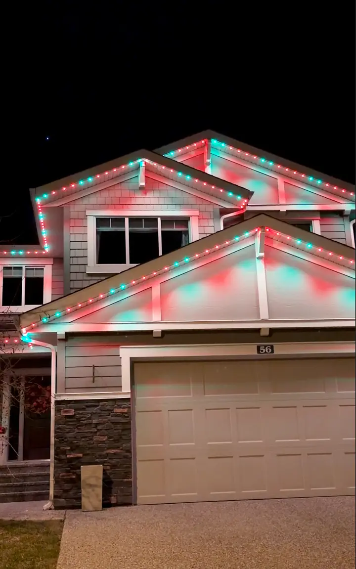 Colourful permanent holiday lights glowing on a snowy Calgary home exterior